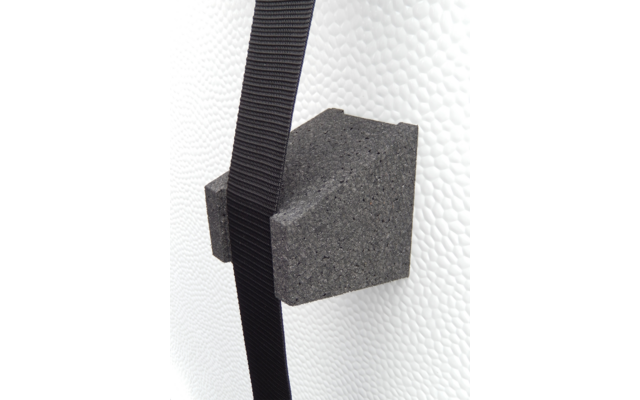 Anthrazitfarbener Schaumstoffblock mit zwei seitlichen Einschnitten auf weißer, genoppter Oberfläche; schwarzer Gurt verläuft davor