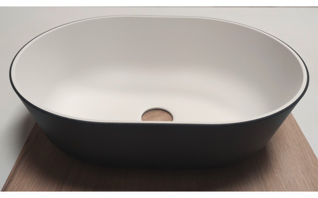 Oval basin with white interior and dark exterior, round wooden plug in drain, on wooden board, light background