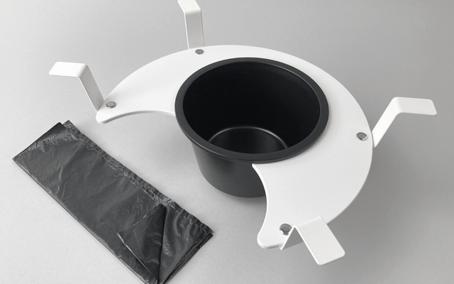 Zwarte plastic zak naast een witte ronde standaard met een zwart inzetstuk op een grijze achtergrond