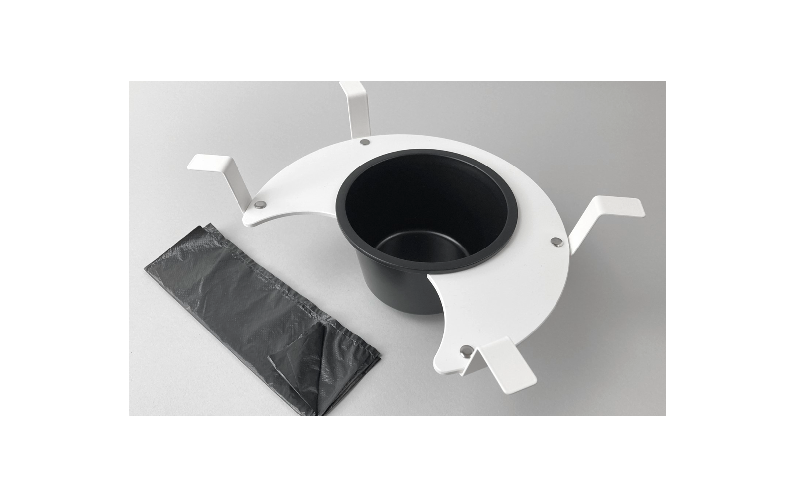 Zwarte plastic zak naast een witte ronde standaard met een zwart inzetstuk op een grijze achtergrond