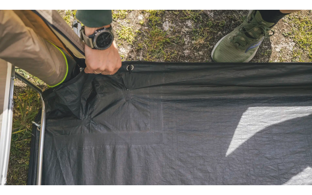 Person hält eine Plane oder ein Zeltgestänge mit zwei Händen am Boden