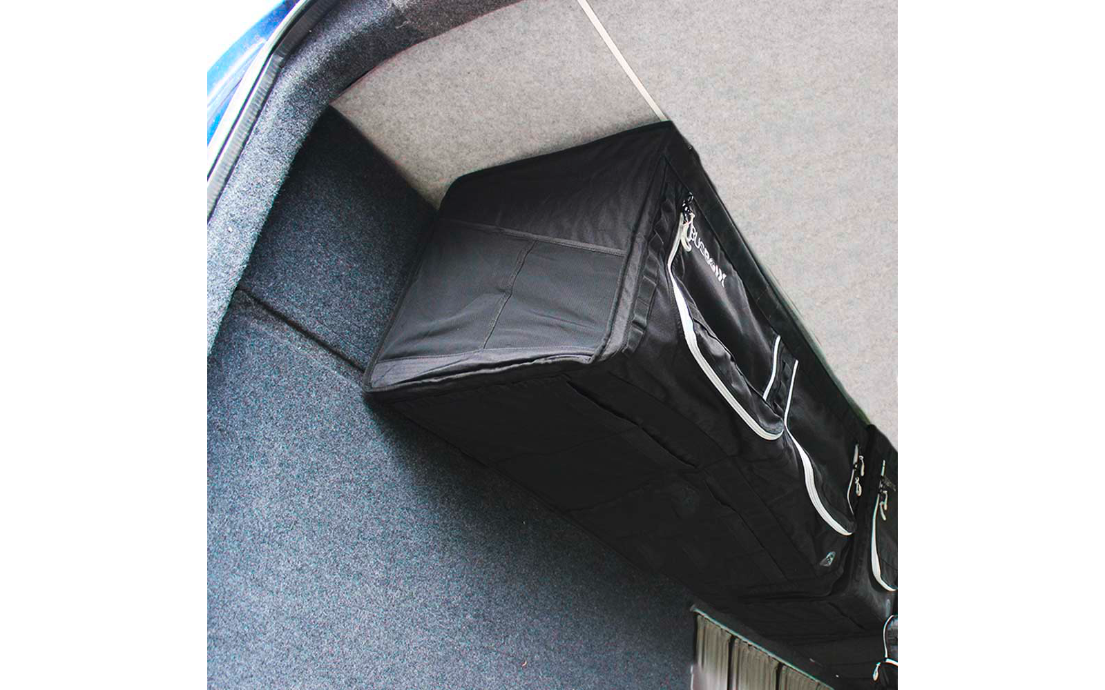 Schwarze rechteckige Aufbewahrungstasche mit weißen Reißverschlüssen, an einer grau bezogenen Fahrzeugdecke befestigt; blauer Fahrzeugrand seitlich sichtbar