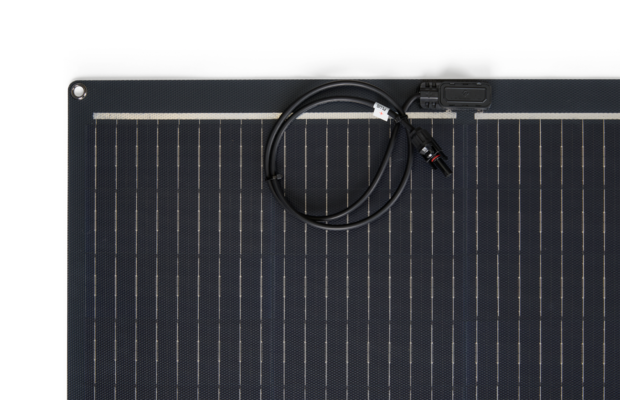 Top portion of a dark solar panel with cell lines, coiled cable with connector at top, metal eyelet in left corner, white background