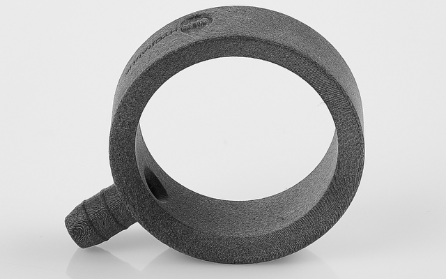 Objeto anular gris oscuro con una corta protuberancia acanalada en el lado exterior, sobre fondo blanco