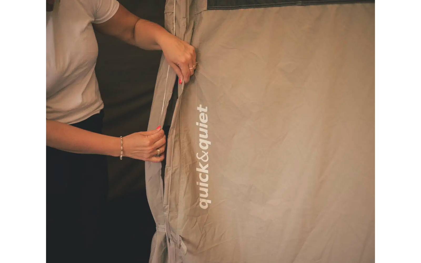 Person öffnet Reißverschluss an hellbraunem Zeltstoff mit Aufdruck quick&quiet