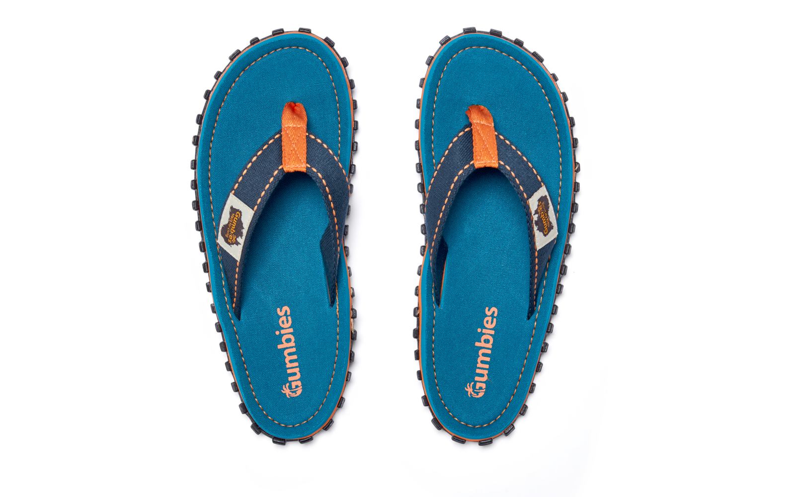 Two blue flip-flops side by side, top view, orange strap accents, Gumbies text on the insoles, black tread soles visible, white tag on the strap