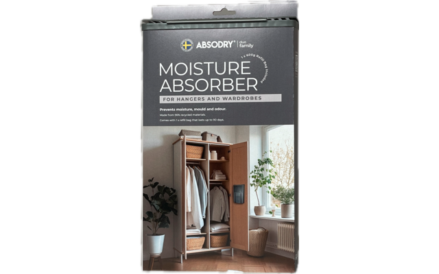 Packung mit Luftentfeuchter vor weißer Wand und Holzboden, daneben Pflanzen und Garderobe