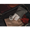 Open koffer met opgevouwen kleding (beige kabelgebreide trui, rood bovenstuk, bordeaux kledingstuk) en een grijs stoffen zakje waar een wit voorwerp met kabel uitsteekt