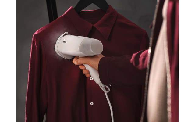 Hand houdt witte kledingstomer met AEG-logo tegen een donkerrood hangend overhemd aan een zwarte hanger