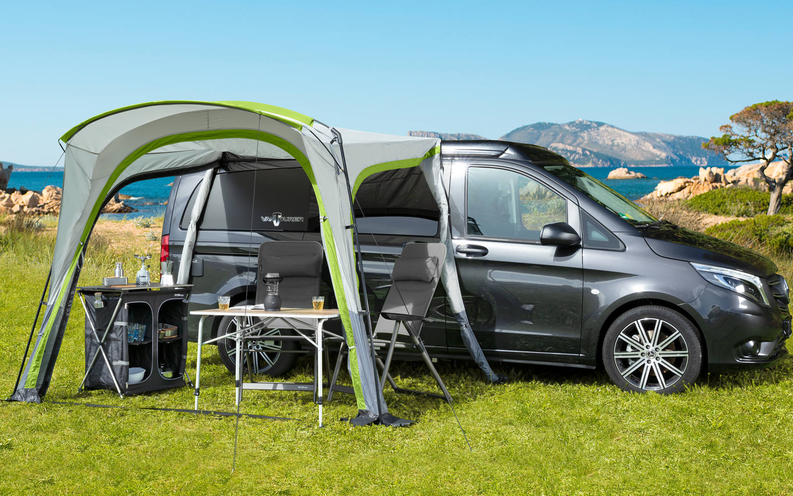 Wohnmobil mit angebautem Vorzelt auf einer grünen Wiese unter klarem blauem Himmel