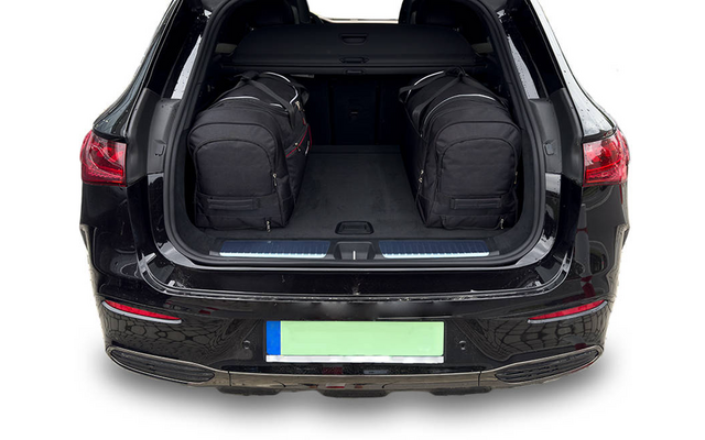 Coffre ouvert d'une voiture noire avec deux sacs de voyage noirs et une plaque d'immatriculation visible