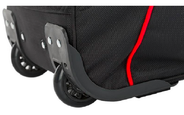 Gros plan du coin inférieur d'une valise en tissu noir avec passepoil rouge, deux roues noires et une protection d'angle en plastique