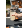 Hand hält ein Glas mit Milch vor einem gedeckten Frühstückstisch