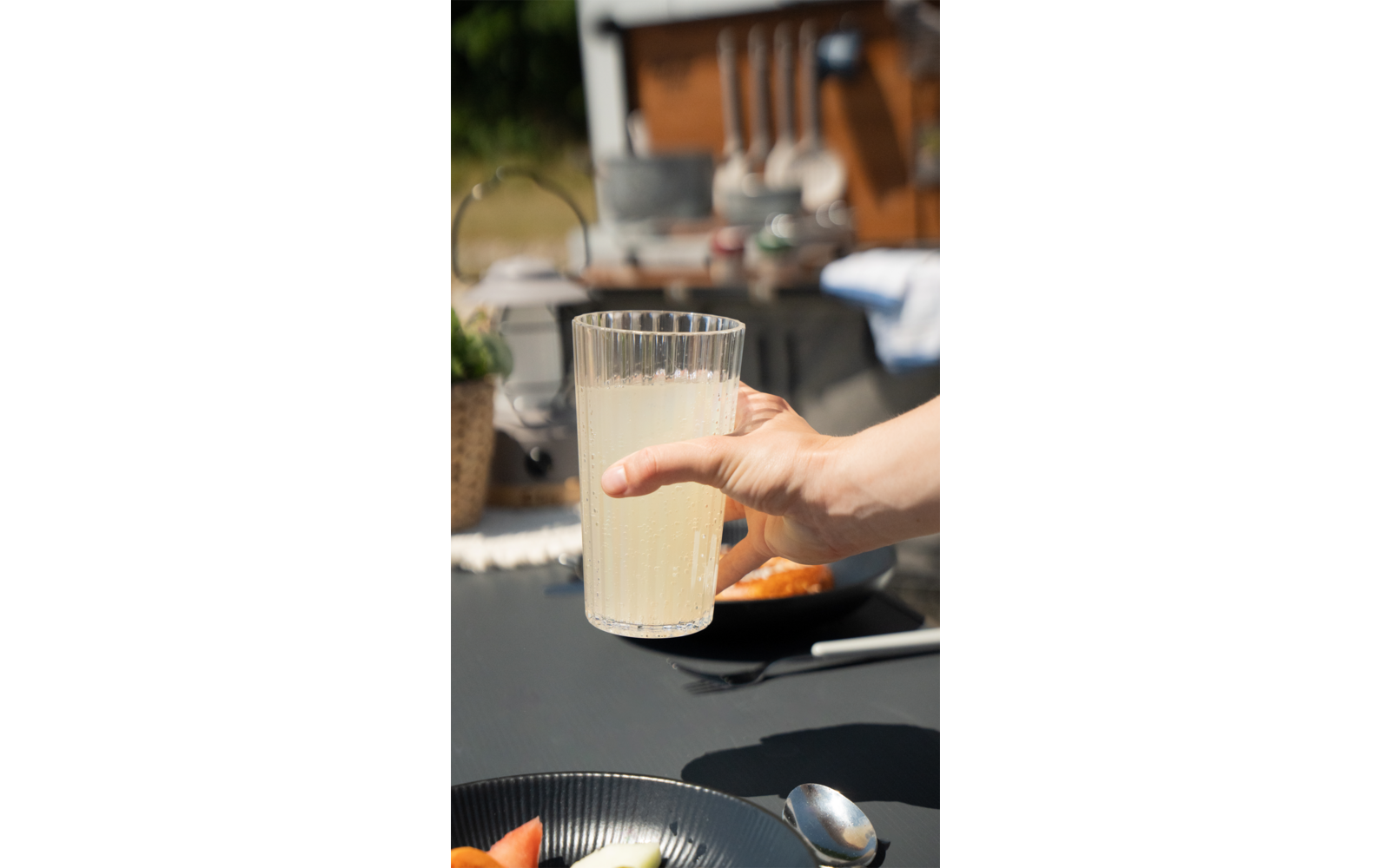 Hand hält ein Glas mit Milch vor einem gedeckten Frühstückstisch