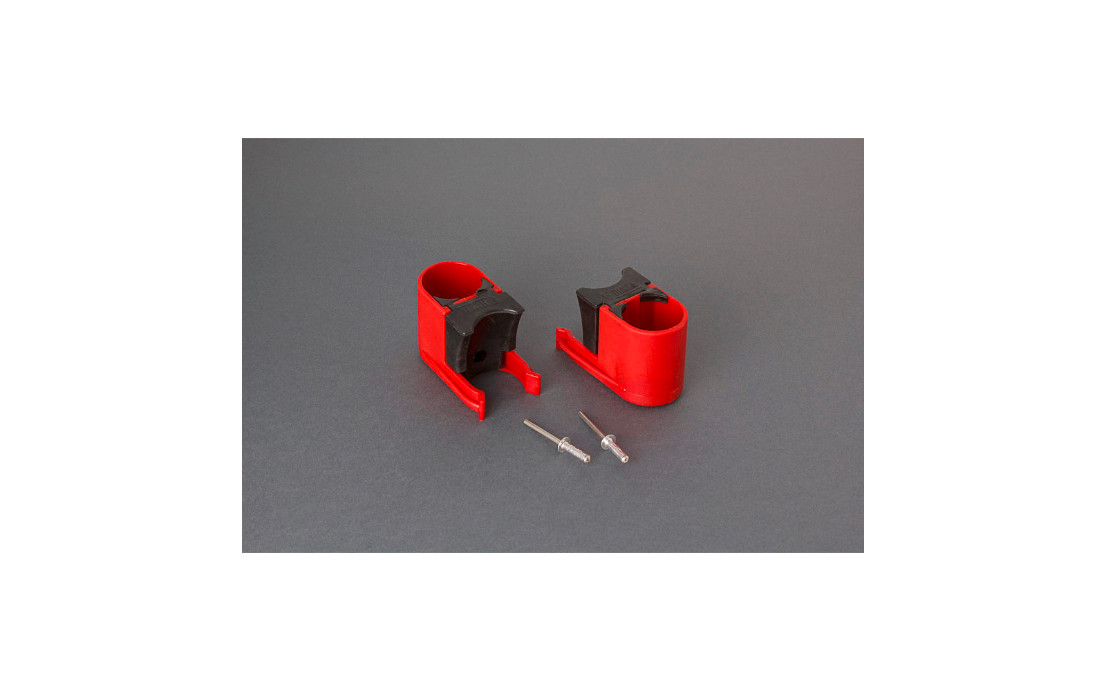 Zwei rote Kunststoffhalter mit schwarzen Einlagen und zwei kleine Spritzen auf grauem Hintergrund