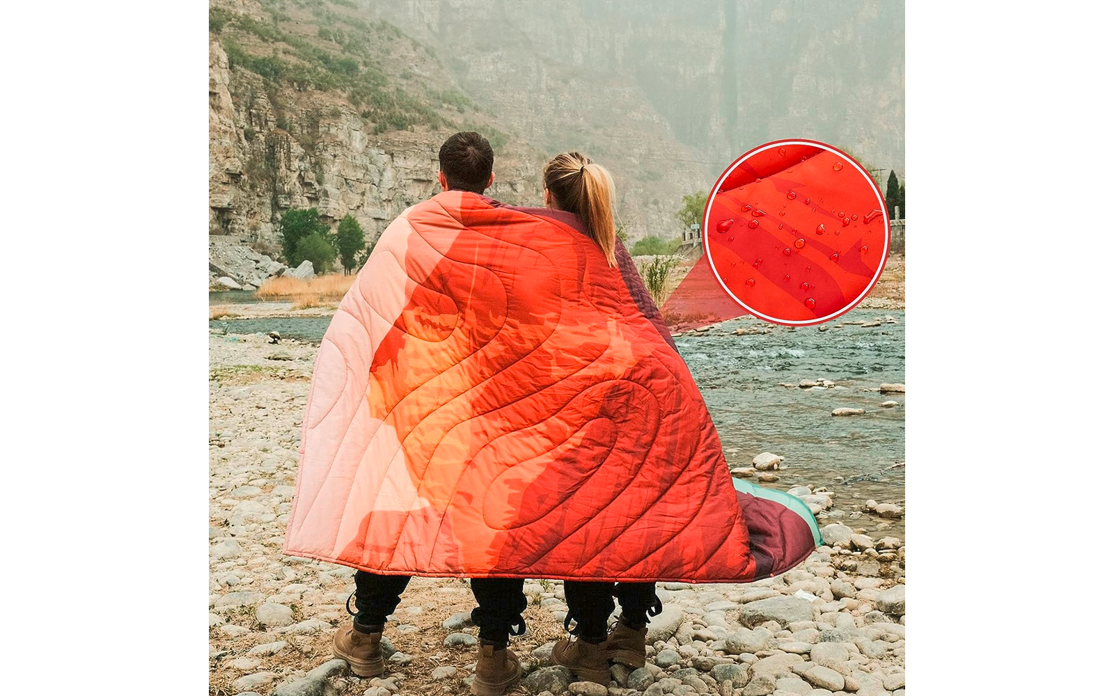 Zwei Personen sitzen auf Steinen an einem Fluss, sie sind mit einer roten Decke bedeckt