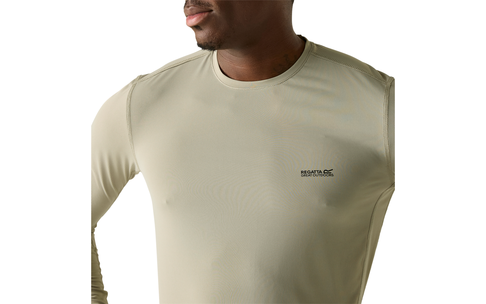 Unterer Teil des Gesichts und Oberkörper einer Person, beiges langärmliges Shirt mit kleinem schwarzem Logodruck auf der linken Brust