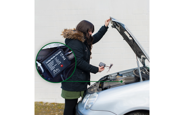 Person mit Winterjacke benutzt Diagnosegerät an offenem Motorraum eines Autos