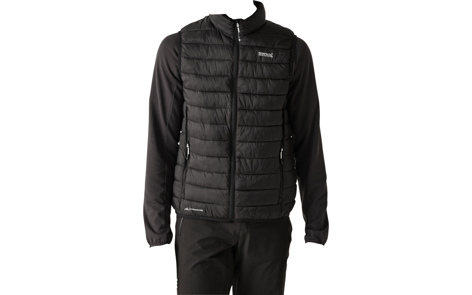 Persona che indossa un gilet imbottito nero sopra una maglia nera a maniche lunghe e pantaloni neri, in piedi davanti a uno sfondo chiaro uniforme, guarda verso sinistra, mani lungo i fianchi