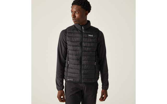 Person trägt schwarze gesteppte Weste über schwarzem Langarmshirt und schwarze Hose, steht vor hellem einfarbigem Hintergrund, schaut nach links, Hände an den Seiten