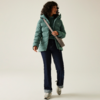 Frau mit lockigem Haar trägt eine grüne Steppjacke, dunkle Hose und weiße Schuhe, sie hält eine braune Tasche auf der Schulter