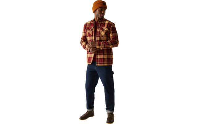 Ein Mann steht vor hellem Hintergrund, trägt eine orangene Mütze, eine kariertes Hemdjacke und dunkle Hose