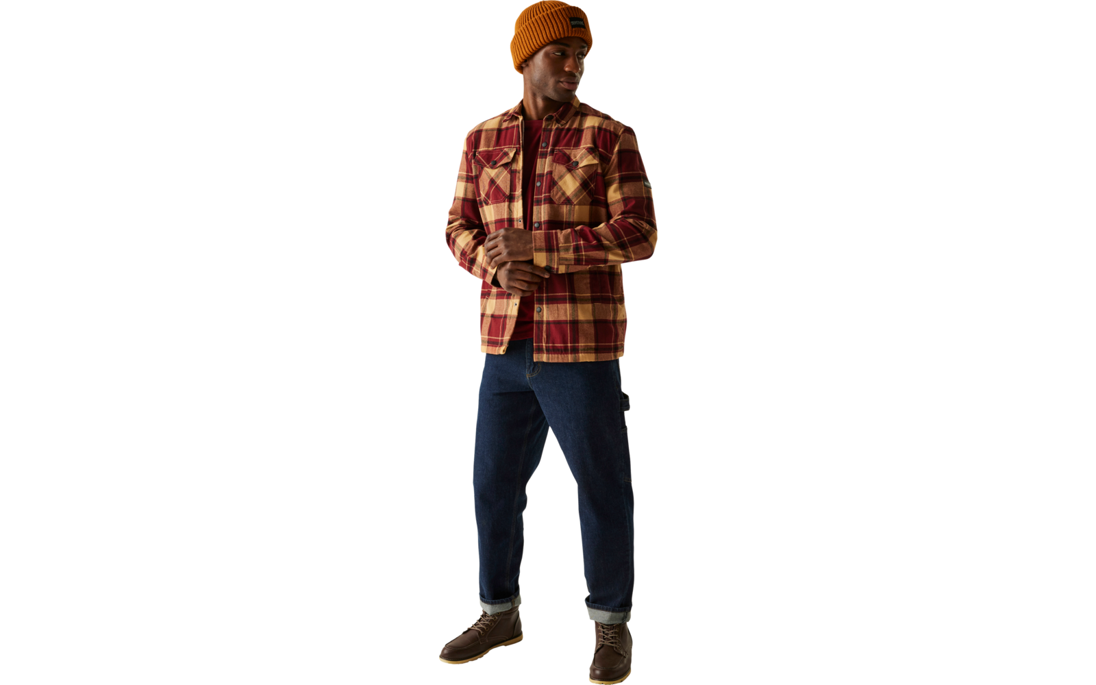 Ein Mann steht vor hellem Hintergrund, trägt eine orangene Mütze, eine kariertes Hemdjacke und dunkle Hose