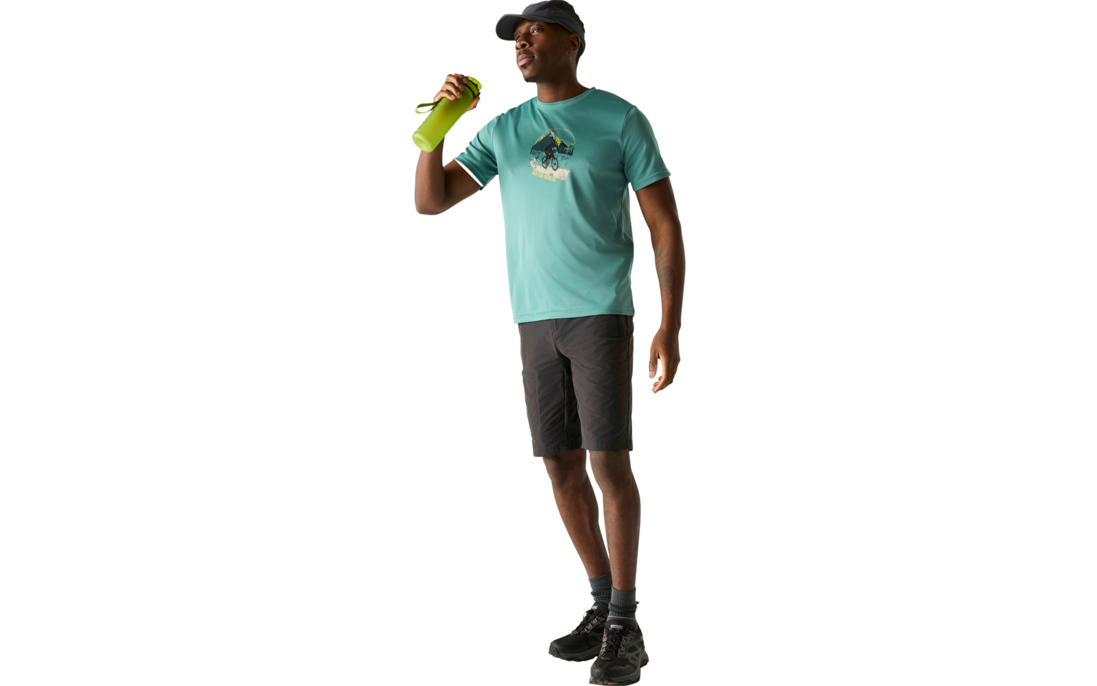 Person steht vor hellem Hintergrund, trägt türkisfarbenes T‑Shirt mit Motiv, schwarze Shorts, Kappe und Schuhe, hält grüne Trinkflasche nahe dem Gesicht, schaut nach rechts