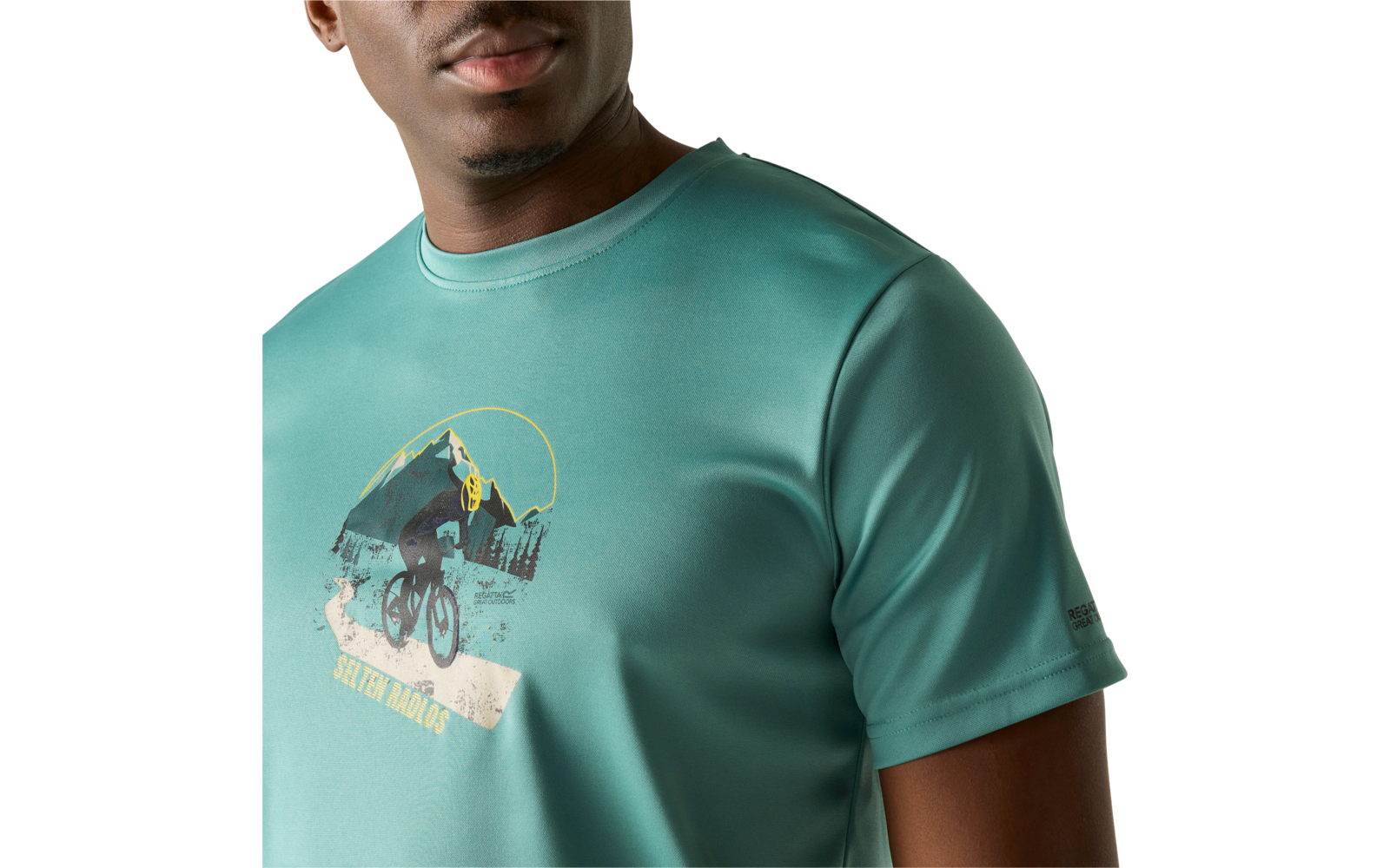 Oberkörper einer Person, Gesicht bis zum Mund teilweise sichtbar; trägt ein türkisgrünes T‑Shirt mit Aufdruck: Bergszene, Fahrradfahrer und gelber Halbkreis