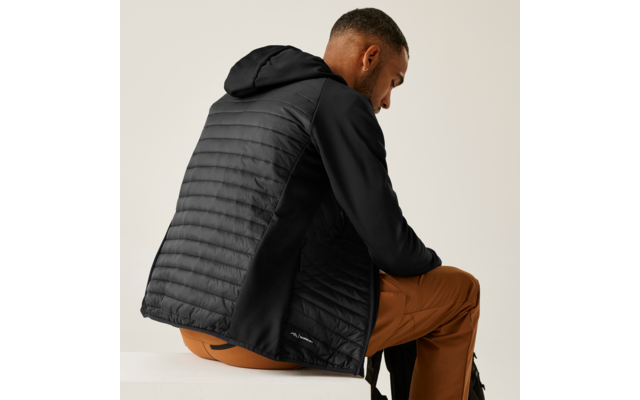 Sitzende Person, zur Seite gewandt, trägt schwarze Kapuzenjacke mit gesteppter Rückenpartie und braune Hose, heller Hintergrund