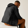 Mann sitzt seitlich, trägt eine schwarze Steppjacke und braune Hose
