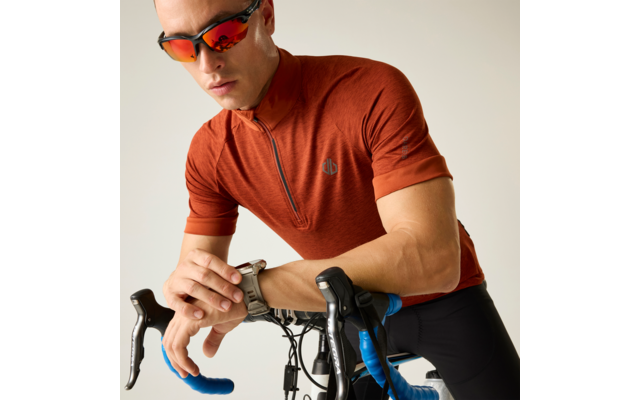 Mann in orangefarbenem Radtrikot mit Sonnenbrille lehnt sich auf den Lenker eines Rennrads und blickt auf seine Uhr