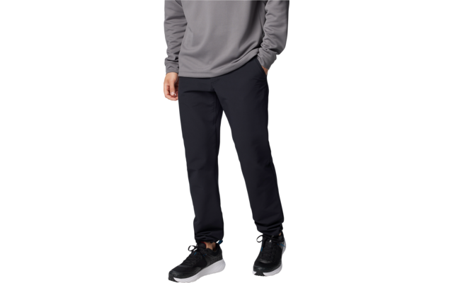 Unterkörper einer Person mit grauem Pullover, schwarzen Hosen und schwarzen Sportschuhen