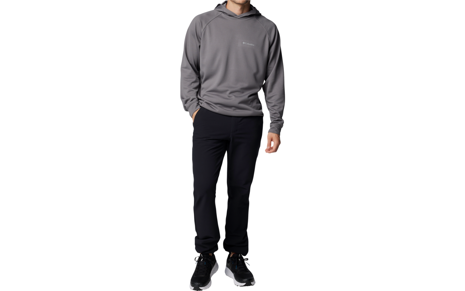 Mann in grauem Pullover und dunkler Hose steht vor weißem Hintergrund