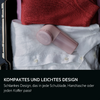 Geöffneter Koffer mit rotem Pullover, weißem Hemd und kleinem rosa Gerät auf dem Hemd; schwarzer Balken mit Text unten