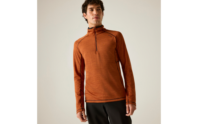 Un homme porte un pull orange à manches longues avec une fermeture éclair jusqu'à la poitrine et un pantalon noir devant un fond uni et clair