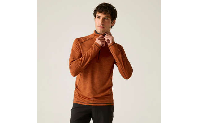 Personne aux cheveux courts et foncés porte un haut à manches longues orange avec une demi-fermeture éclair et un pantalon foncé, tire sur la fermeture; fond uni clair