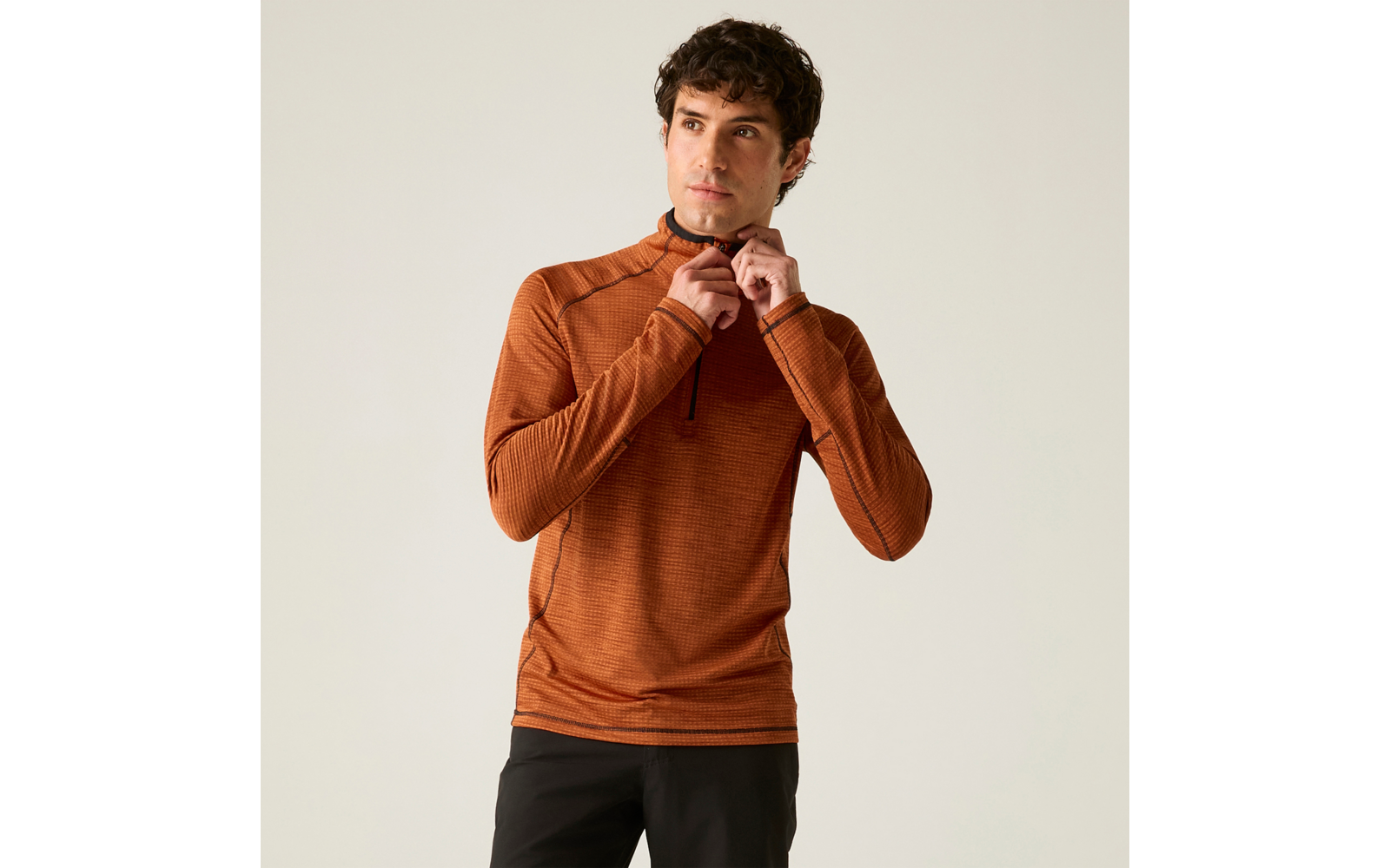 Personne aux cheveux courts et foncés porte un haut à manches longues orange avec une demi-fermeture éclair et un pantalon foncé, tire sur la fermeture; fond uni clair