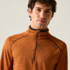 Personne aux cheveux bruns et bouclés, portant un haut de sport orange texturé avec une courte fermeture éclair, fond uni lumineux