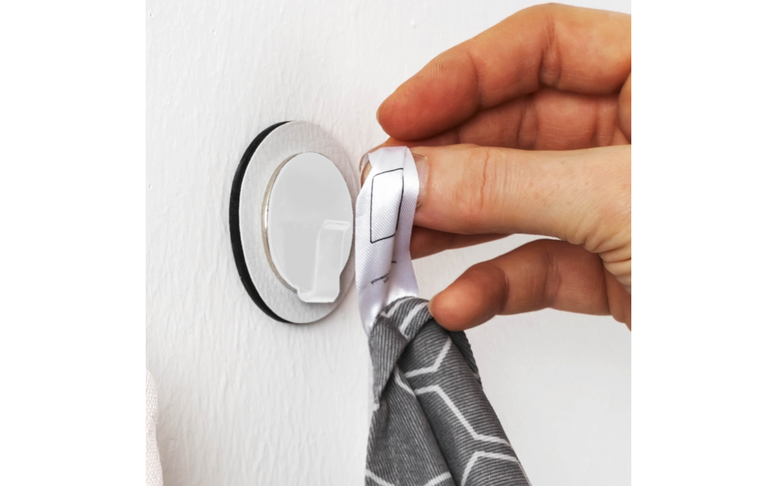 Hand hängt ein graues Tuch an einen weißen selbstklebenden Haken an der Wand