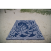 Serviette de plage rectangulaire bleue à motif, posée à plat sur du sable clair; herbe des dunes en haut