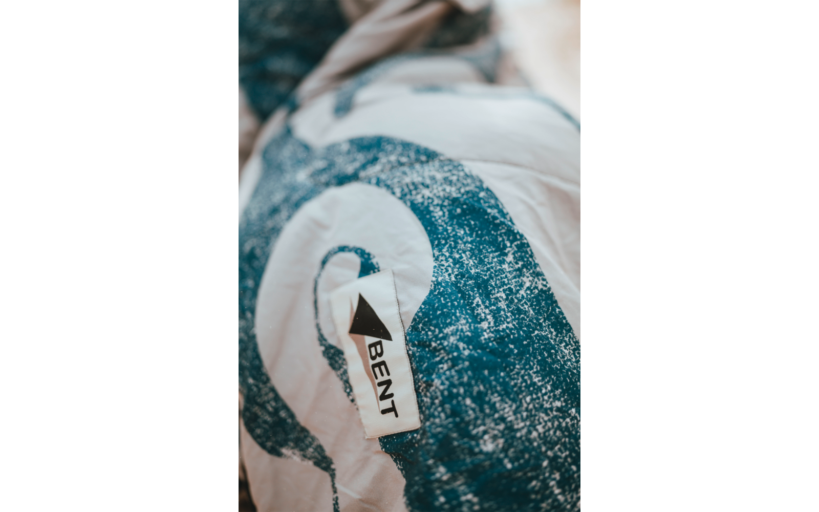 Gros plan sur un tissu blanc à motif spiral bleu et une étiquette cousue portant la mention "BENT"