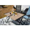 Klapptisch mit zwei hohen Gläsern mit bernsteinfarbener Flüssigkeit und Schaum, Marmeladenglas mit Löffel, kleine Dose, Topf mit Pflanze, zwei Campingklappstühle neben einem Wohnmobil auf einer gemusterten Decke