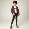 Mädchen steht vor hellem Hintergrund, trägt violette Jacke, hellrosa Sweatshirt mit Bergmotiv, schwarze Leggings, braune Wanderschuhe und -socken, hochgesteckte lockige Haare, lächelt