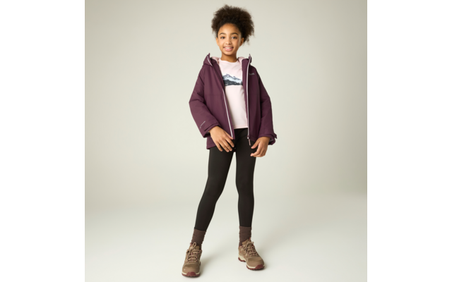 Mädchen steht vor hellem Hintergrund, trägt violette Jacke, hellrosa Sweatshirt mit Bergmotiv, schwarze Leggings, braune Wanderschuhe und -socken, hochgesteckte lockige Haare, lächelt