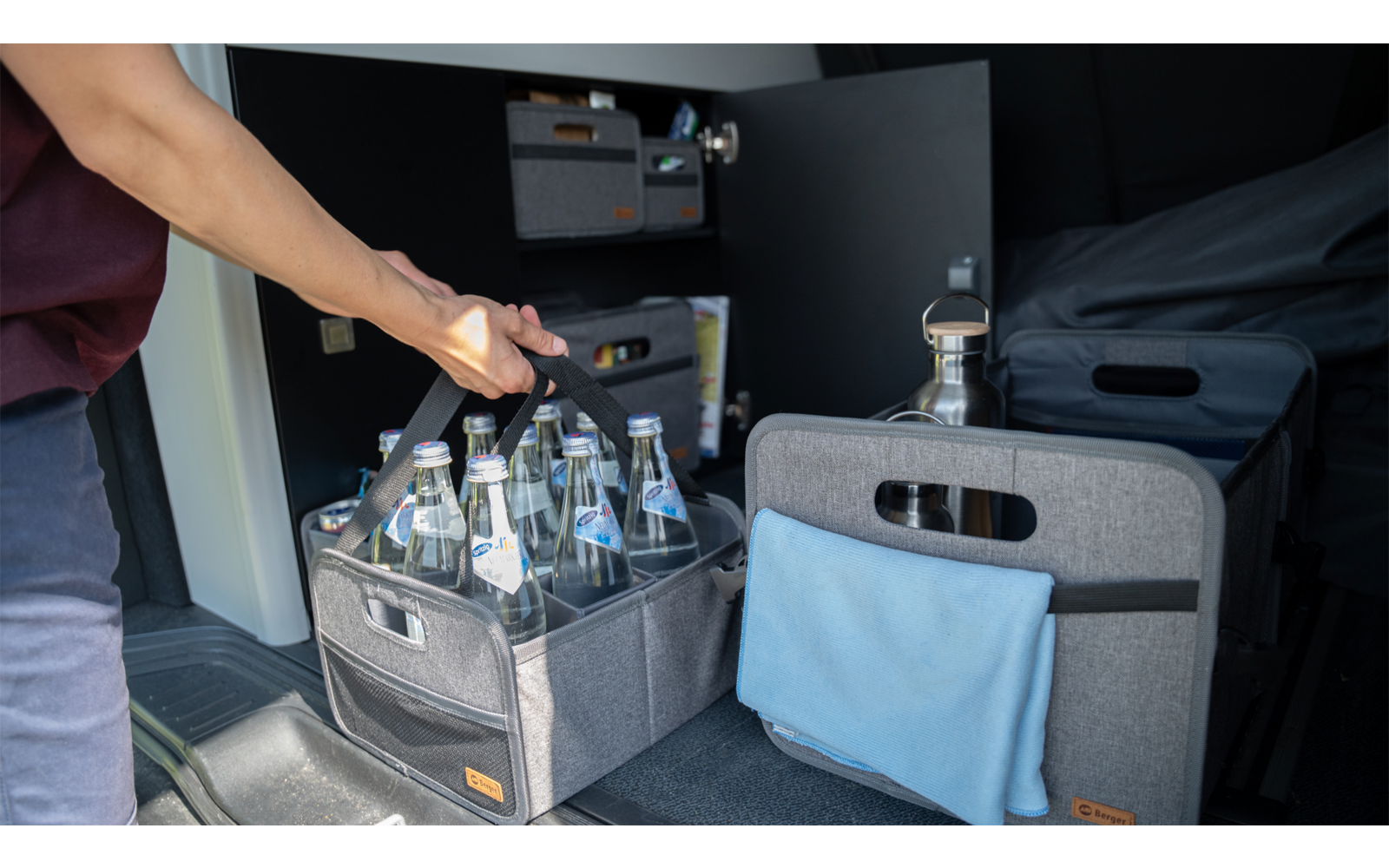 Personne tenant une caisse avec plusieurs bouteilles près d'une machine à café et d'un coin salon