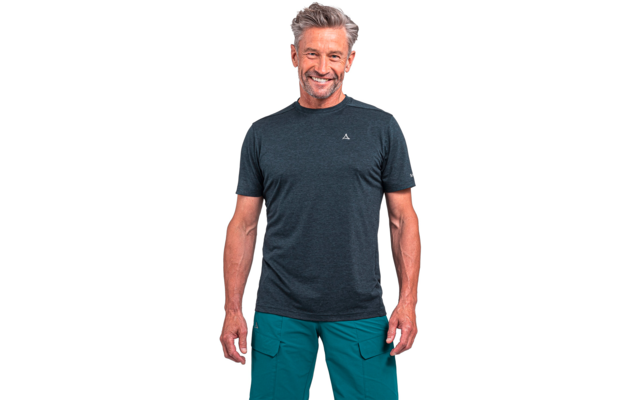 Stehender Mann mit kurzen grauen Haaren, dunkelgrauem T-Shirt mit kleinem Logo auf der Brust und grünen Cargohosen vor weißem Hintergrund