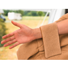 Uitgestrekte onderarm en hand naast een mouw van een beige jas; wazig grasveld en een caravan op de achtergrond