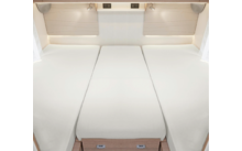 Drei nebeneinander liegende Einzelbetten mit weißen Matratzen in einem hellen Raum