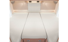 Trois lits simples avec des matelas blancs placés côte à côte dans une pièce lumineuse